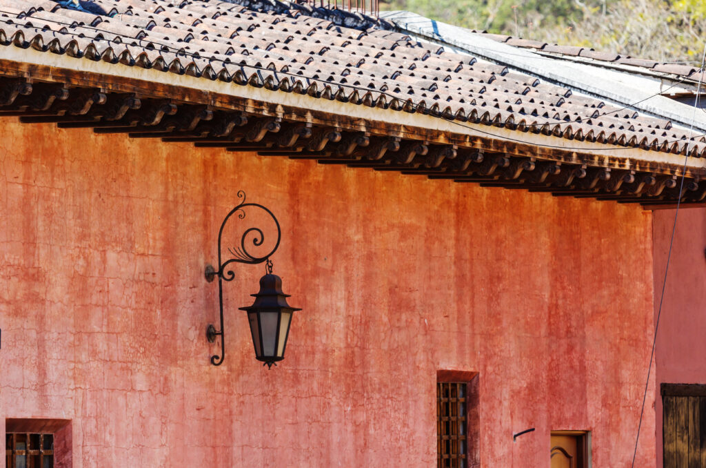 Pared colonial de color terracota con techo de teja y un farol de hierro forjado en Antigua Guatemala